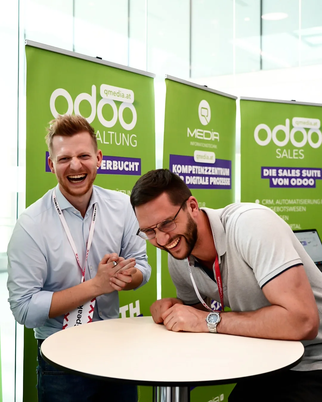 Christoph Fischer and Alexander Umgeher laughing at the QMedia IT trade fair stand